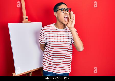 Un jeune afro-américain, debout par le peintre chevalet, criait et criait à voix haute à côté de la main sur la bouche. Concept de communication. Banque D'Images