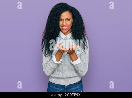 Femme afro-américaine d'âge moyen portant des vêtements décontractés souriant avec les mains paumes ensemble recevoir ou donner des gestes. Tenir et protection Banque D'Images