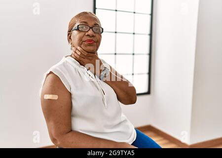 Femme hispanique mature qui obtient le vaccin montrant le bras avec l'aide de bande touchant le cou douloureux, mal de gorge pour la grippe, la motte et l'infection Banque D'Images