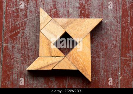 Puzzle Tangram en forme de shuriken sur fond de vieux bois rouge Banque D'Images