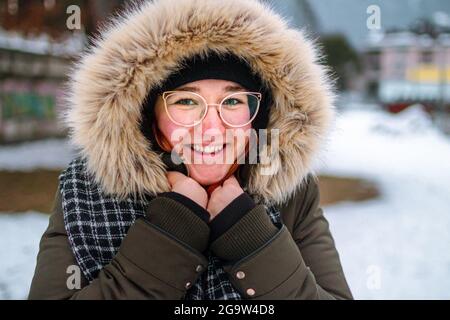 Bonne jeune femme souriant et protégeant sa main contre le froid sous une veste fourrure en hiver comme elle a oublié de porter des gants Banque D'Images