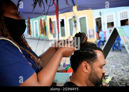 salvador, bahia, brésil - 27 juillet 2021: Coiffeur est vu braiding des cheveux touristiques à Pelourinho, centre historique de la ville de Salvador. Banque D'Images