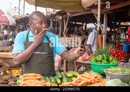 Photo de stock de l'épicerie africaine masculine avec un tablier, étonné comme il se tient et fixe à son téléphone Banque D'Images