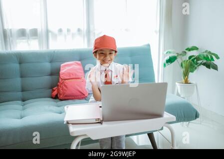 élève de l'école primaire avec uniforme agitant à son professeur et ami pendant la session de classe en ligne Banque D'Images