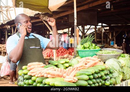 Photo d'un vendeur d'épicerie africain masculin avec tablier, heureux de faire un appel avec un smartphone Banque D'Images