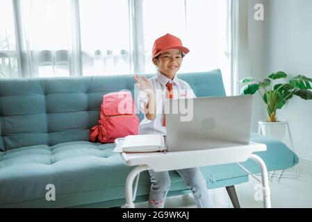 élève de l'école primaire avec uniforme agitant à son professeur et ami pendant la session de classe en ligne Banque D'Images