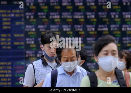 Tokyo, Japon. 24 juin 2021. Les personnes portant des masques de visage comme mesure préventive contre la propagation de Covid-19 marchent au-delà d'un écran affichant les indices de la moyenne de Nikkei et de la bourse mondiale en dehors d'une maison de courtage, dans le cadre de l'épidémie de coronavirus (COVID-19), à Tokyo. (Image de crédit : © James Matsumoto/SOPA Images via ZUMA Press Wire) Banque D'Images