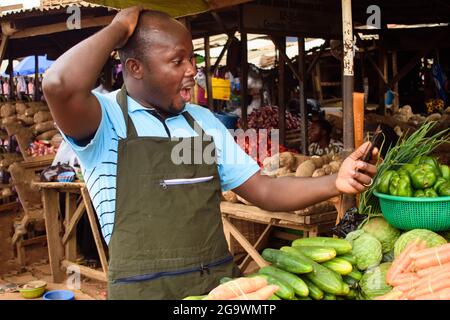 Photo de stock de l'épicerie africaine masculine avec un tablier, étonné comme il se tient et fixe à son téléphone Banque D'Images