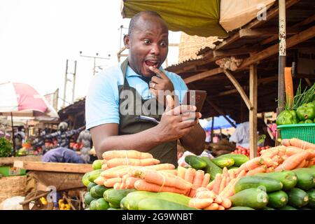 Photo de stock de l'épicerie africaine masculine avec un tablier, étonné comme il se tient et fixe à son téléphone Banque D'Images