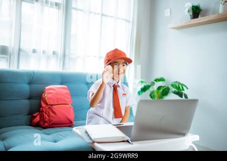 élève de l'école primaire avec uniforme agitant à son professeur et ami pendant la session de classe en ligne Banque D'Images