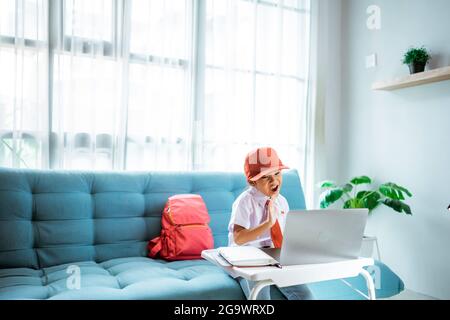 élève de l'école primaire avec uniforme agitant à son professeur et ami pendant la session de classe en ligne Banque D'Images