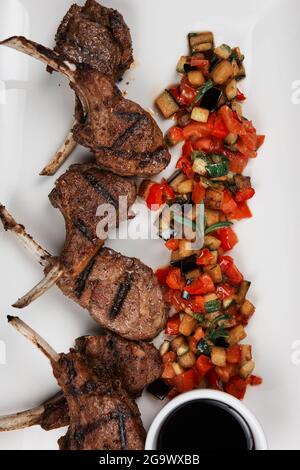 Côtes d'agneau grillées aux légumes sur plaque blanche sur fond de bois noir Banque D'Images