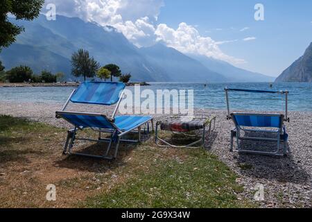 Transats vides avec vue sur le lac et la montagne, plage en pierre à Riva del Garda Banque D'Images