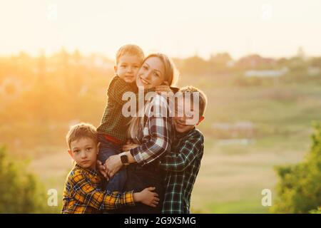 Une mère heureuse et son trois fils jouent au coucher du soleil. Concept familial convivial. Pour explorer la nature en soirée sous le soleil chaud jour d'été. Passez du temps ensemble Banque D'Images