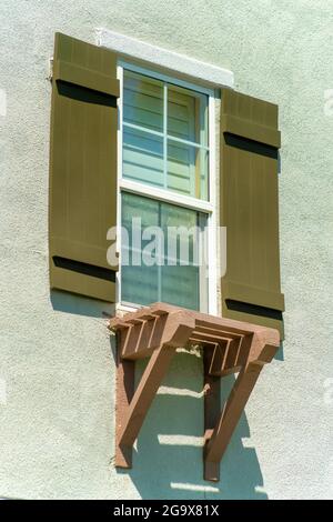 Plan vertical d'une fenêtre avec un cadre blanc et des volets peints en marron sur un mur gris Banque D'Images
