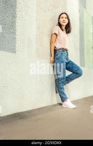 Jeune femme attrayante posant contre un mur en béton. Espace de copie, pleine longueur. Banque D'Images