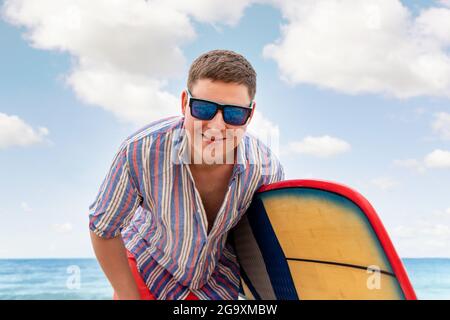 Portrait de jeune adulte élégant homme caucasien porter une chemise décontractée et des lunettes de soleil profiter d'avoir du temps libre surf à l'océan vacances de voyage de bord de mer Banque D'Images