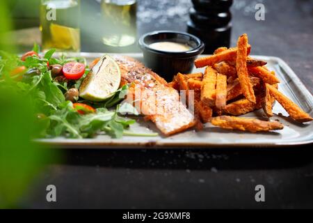 Saumon grillé avec frites de patate douce et salade. Le cuisinier cuisine et sert un plat appétissant. Le plat fini servi sur une assiette. Proposition de service Banque D'Images