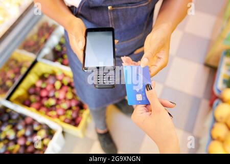 Gros plan de la femme qui paie pour son achat par carte de crédit alors que le vendeur tient le terminal dans la boutique Banque D'Images