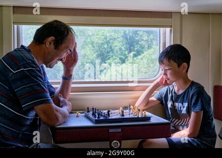 Jeune garçon asiatique et homme senior jouant aux échecs en train. Banque D'Images