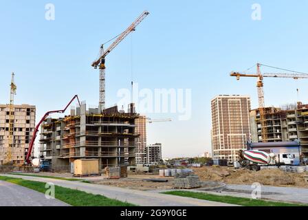 Vue sur le grand chantier de construction. Grues à tour en action. Coffrages et coulage de béton à travers un camion à pompe autonome connecté à un camion prêt à l'emploi Banque D'Images