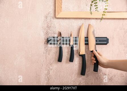 Femme et support magnétique avec couteaux accrochés au mur de couleur Banque D'Images