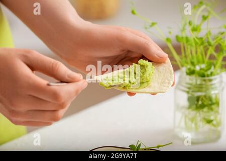 Femme répandant le houmous savoureux de pois verts sur le pita sur fond clair, gros plan Banque D'Images