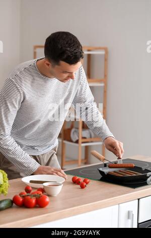 Un jeune homme friture des saucisses savoureuses dans la cuisine Banque D'Images