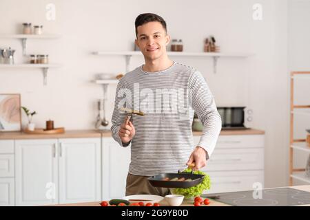 Un jeune homme friture des saucisses savoureuses dans la cuisine Banque D'Images