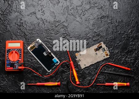 Téléphone mobile démonté avec multimètre sur fond sombre Banque D'Images