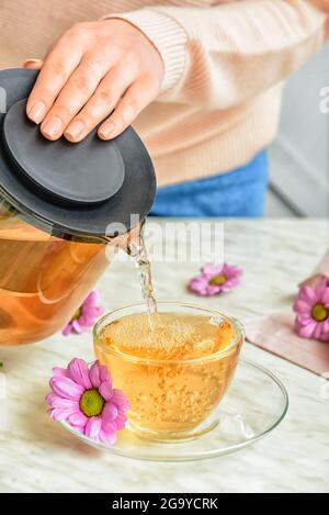 Femme versant le thé de la théière dans la tasse sur la table, gros plan Banque D'Images