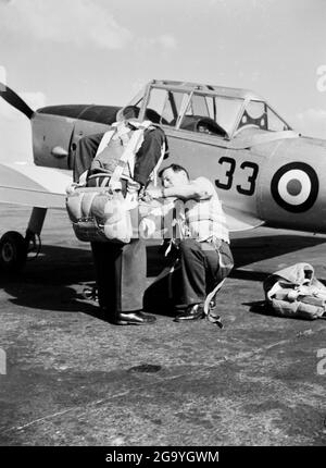 Instructeur ajustant l'équipement volant d'un pilote stagiaire, avec un avion d'entraînement RAF de Havilland Chipmunk derrière lui Banque D'Images