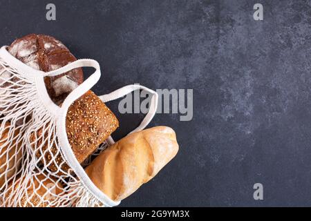 Différents types de pain frais dans un sac fourre-tout blanc en maille sur fond noir vue du dessus. Concept d'éco-shopping. Banque D'Images