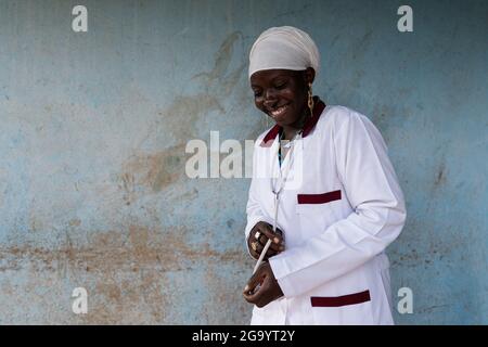 Belle jeune stagiaire afro-médical souriant avec un stéthoscope autour de son cou regardant le sol avec une expression satisfaite sur son visage après le re Banque D'Images