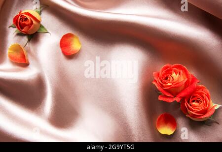 Composition des fleurs. Cadre en roses rouges et feuilles sur fond de soie beige. Vue de dessus, plat, espace de copie Banque D'Images