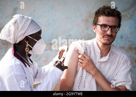 Dans cette image, un jeune adulte du caucase dont l'expression est tendue sur son visage est injecté dans son bras droit une injection de vaccin par une infirmière noire portant un fa Banque D'Images