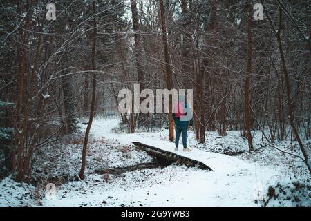 Homme voyageur avec sac à dos debout seul sur un petit pont dans la forêt en hiver Banque D'Images