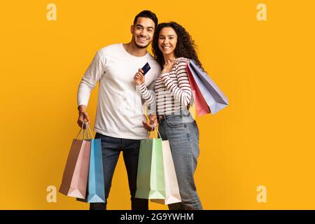 Joyeux jeune couple arabe posant avec la carte de crédit et des sacs de shopping lumineux Banque D'Images