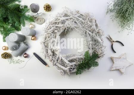 Décorant une couronne de l'Avent en bois blanc avec des branches de feu vertes, des boules de Noël d'or pâle et des bougies grises pour un arrangement naturel d'hiver, h Banque D'Images