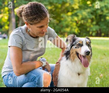 Bonne femme assise en compagnie d'un jeune chien de berger australien dans la prairie Banque D'Images