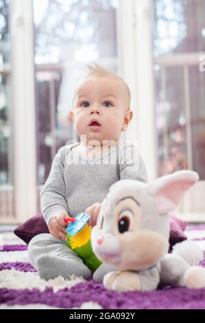 Joyeux bébé garçon assis sur le sol et jouant avec son jouet. Banque D'Images