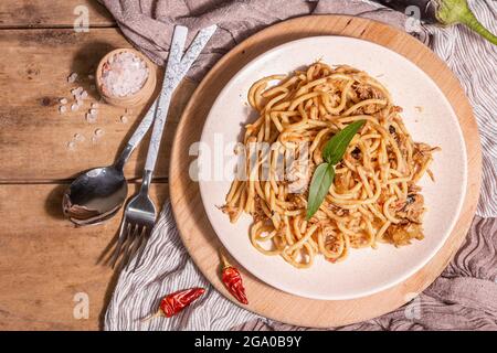 Plat traditionnel de pâtes siciliennes d'aubergines sautées nappées de sauce tomate. Plats servis sur une plaque de céramique, cuisine italienne, lumière dure moderne, sombre Banque D'Images