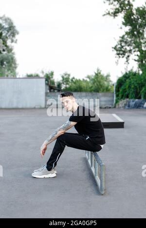 jeune homme brunette assis seul sur un terrain de jeu de patinage en asphalte Banque D'Images