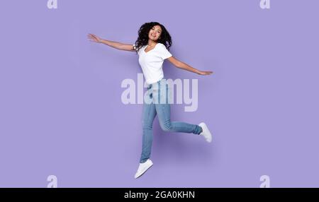 Femme en train de sauter posant en milieu d'air exprimant des émotions positives, fond violet Banque D'Images