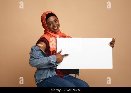 Une femme musulmane afro-américaine joyeuse s'est vaccinée, montrant un écriteau vide Banque D'Images