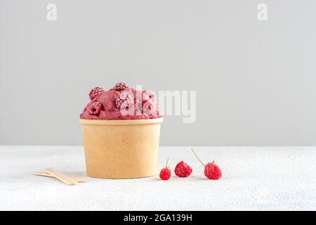 Crème glacée à la framboise rouge et à la banane végétalienne avec framboises congelées dans un bol en papier Banque D'Images