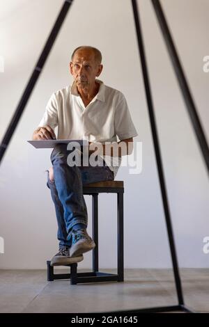 Peintre ou artiste mature ou senior avec crayon graphite devant l'appareil photo. Homme dans une chemise colorée à la peinture travaillant au studio Banque D'Images