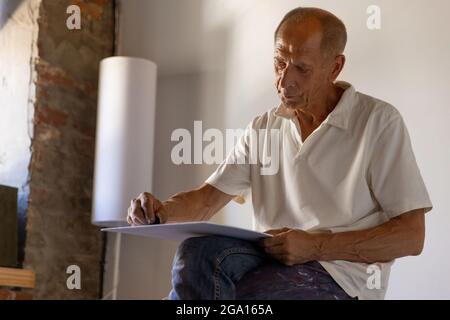 Peintre ou artiste mature ou senior avec crayon graphite devant l'appareil photo. Homme dans une chemise colorée à la peinture travaillant au studio Banque D'Images