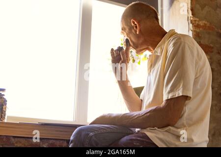 Peintre ou artiste mature ou senior avec crayon graphite devant l'appareil photo. Homme dans une chemise colorée à la peinture travaillant au studio Banque D'Images