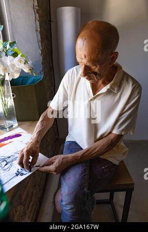 Peintre ou artiste mature ou senior avec crayon graphite devant l'appareil photo. Homme dans une chemise colorée à la peinture travaillant au studio Banque D'Images